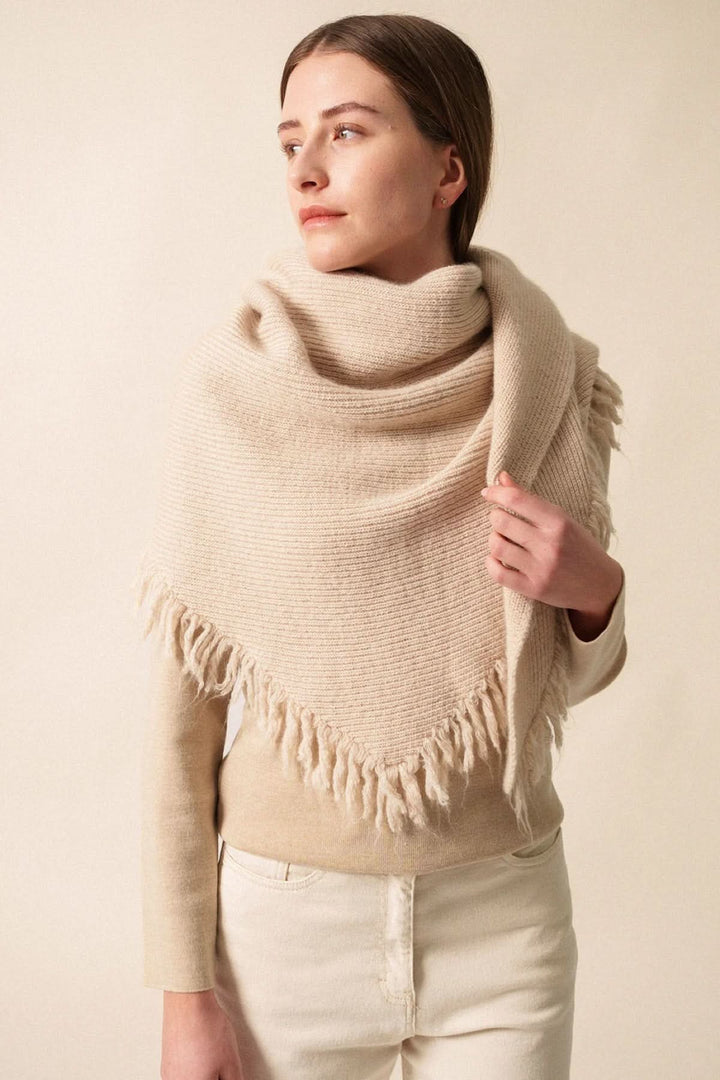 Foulard en maille douce avec franges, porté sur les épaules pour un look élégant et chaleureux.