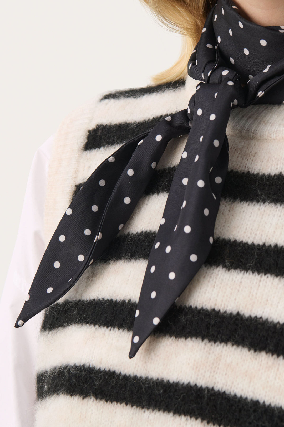 Foulard Lupa à pois noir élégant porté avec un pull rayé, ajoutant une touche féminine et intemporelle.