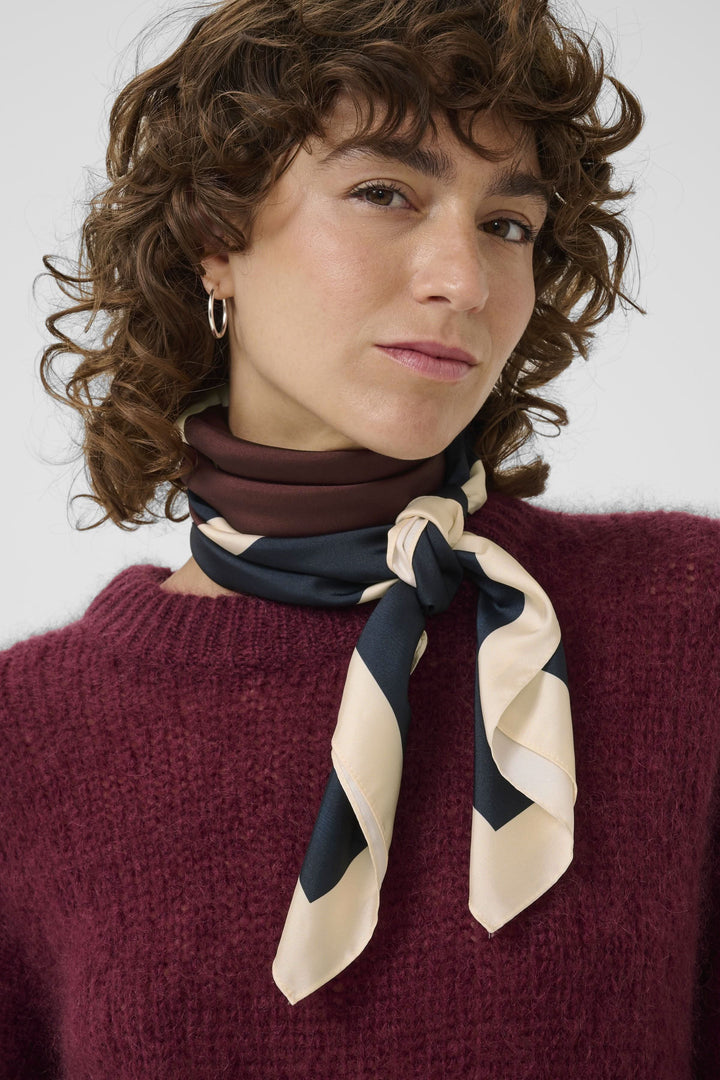 Foulard Namira porté en lavallière, motif bicolore chic sur fond sombre, accessoire élégant pour un look moderne.