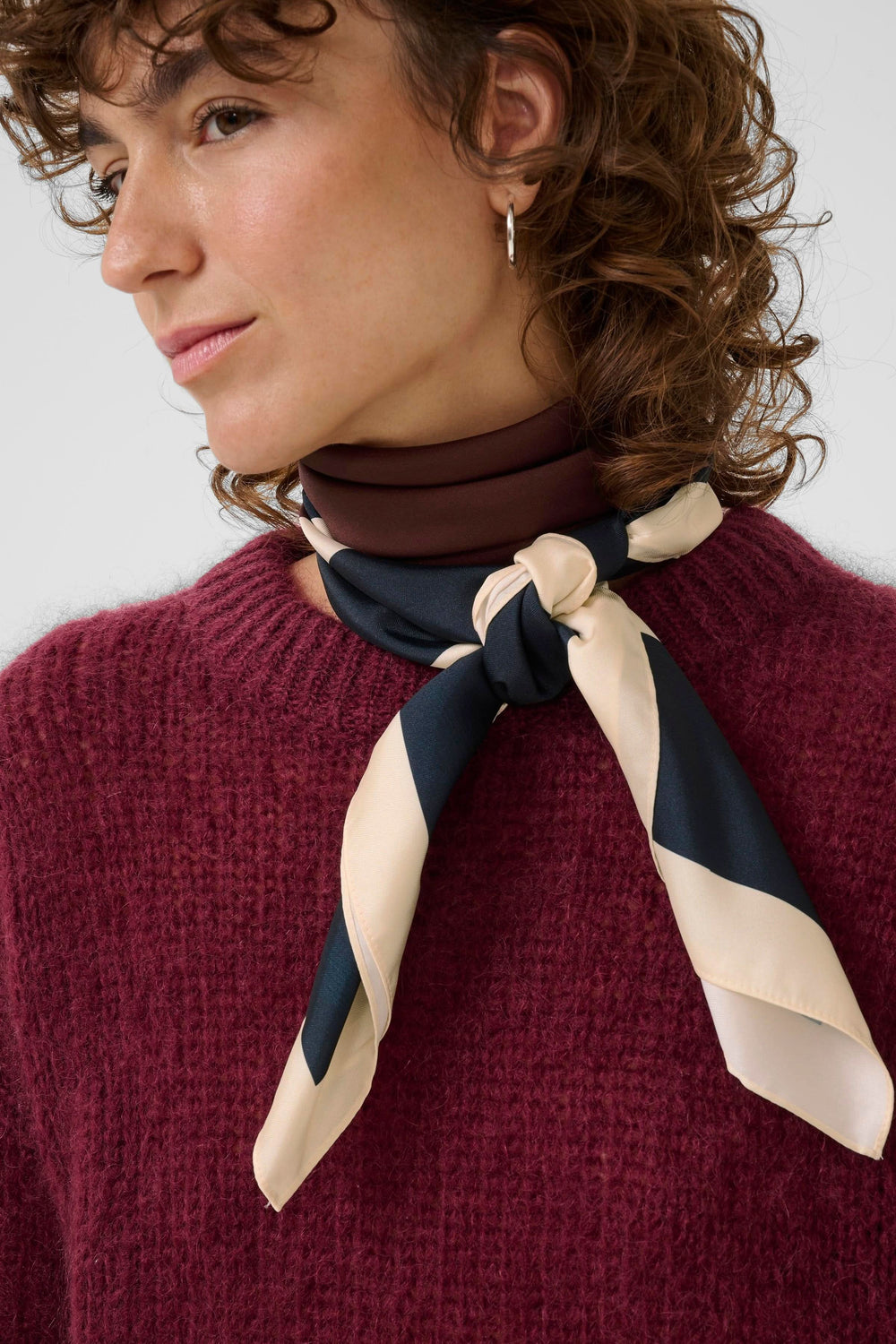 Foulard Namira en motif graphique bicolore porté noué, ajoutant une touche chic à un pull en maille.