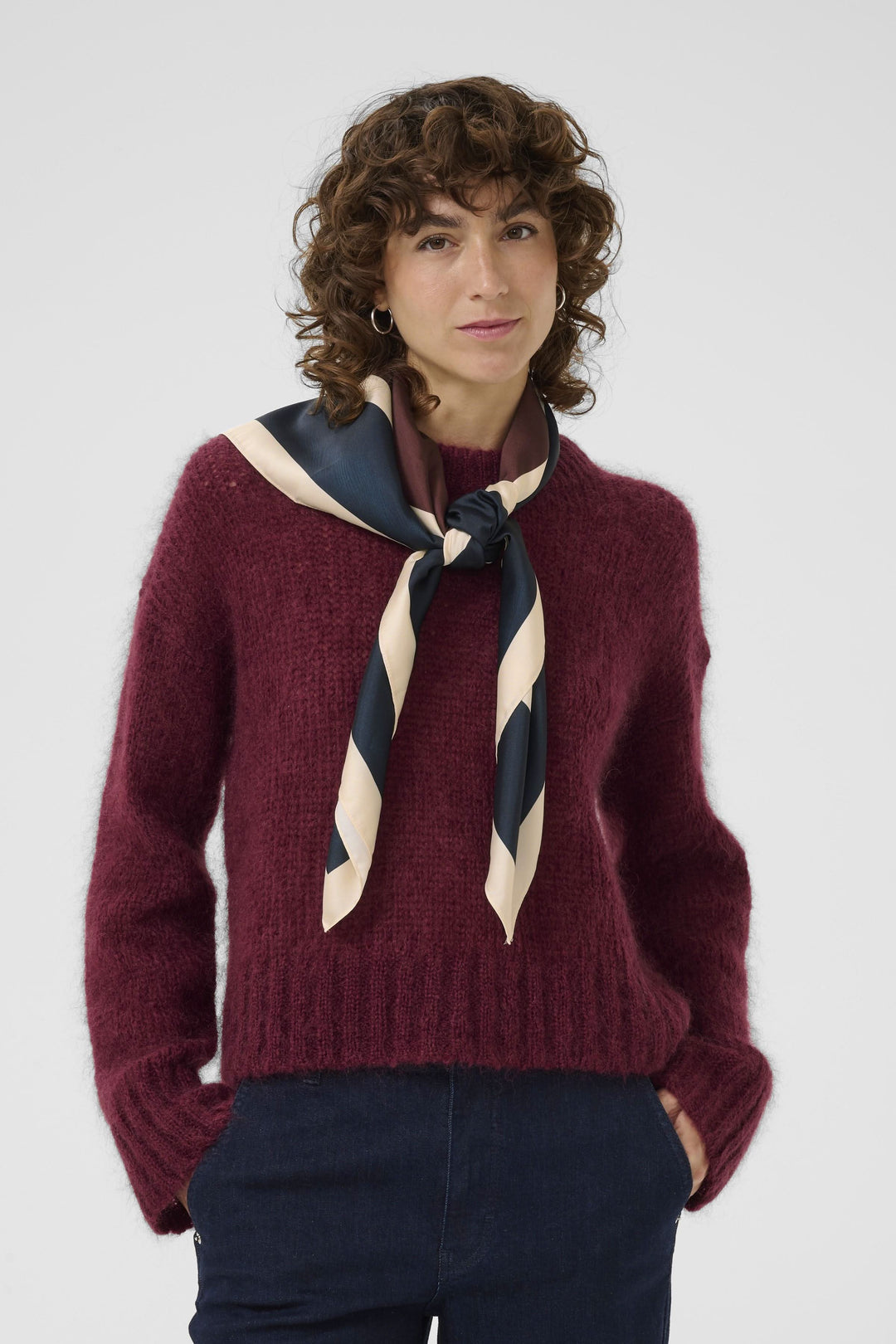 Foulard Namira noué en lavallière sur un pull bordeaux, ajoutant une touche chic et moderne.