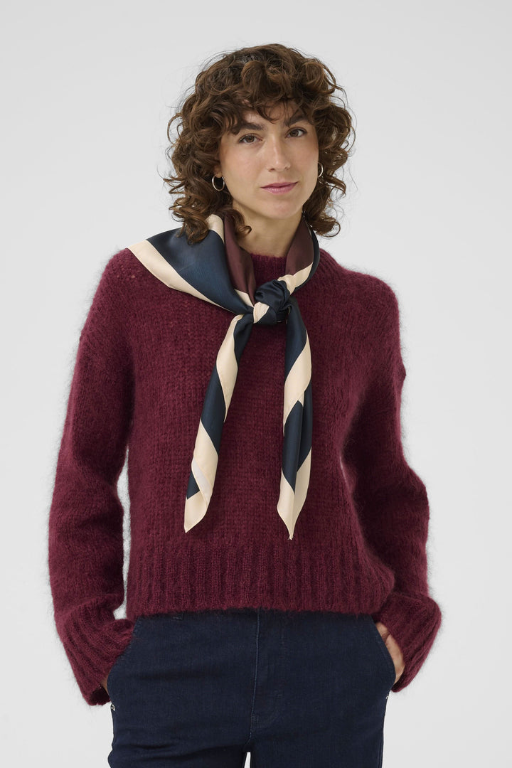 Foulard Namira noué en lavallière sur un pull bordeaux, ajoutant une touche chic et moderne.