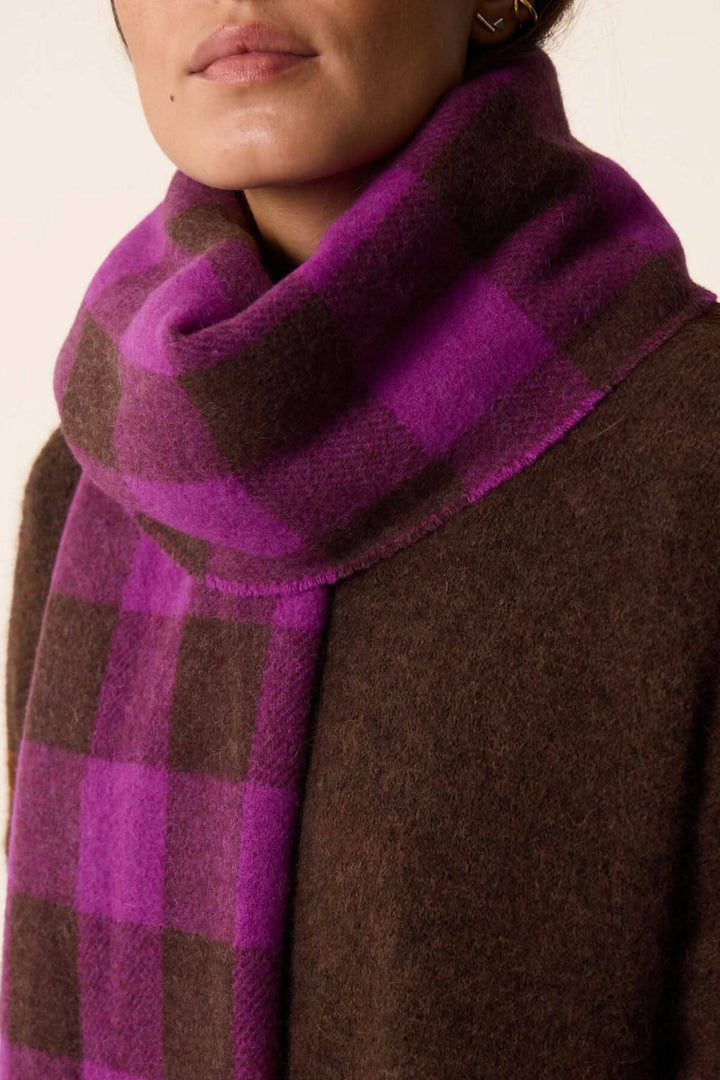 Foulard à carreaux avec des couleurs vives, porté avec un manteau marron pour un look chic et chaleureux.