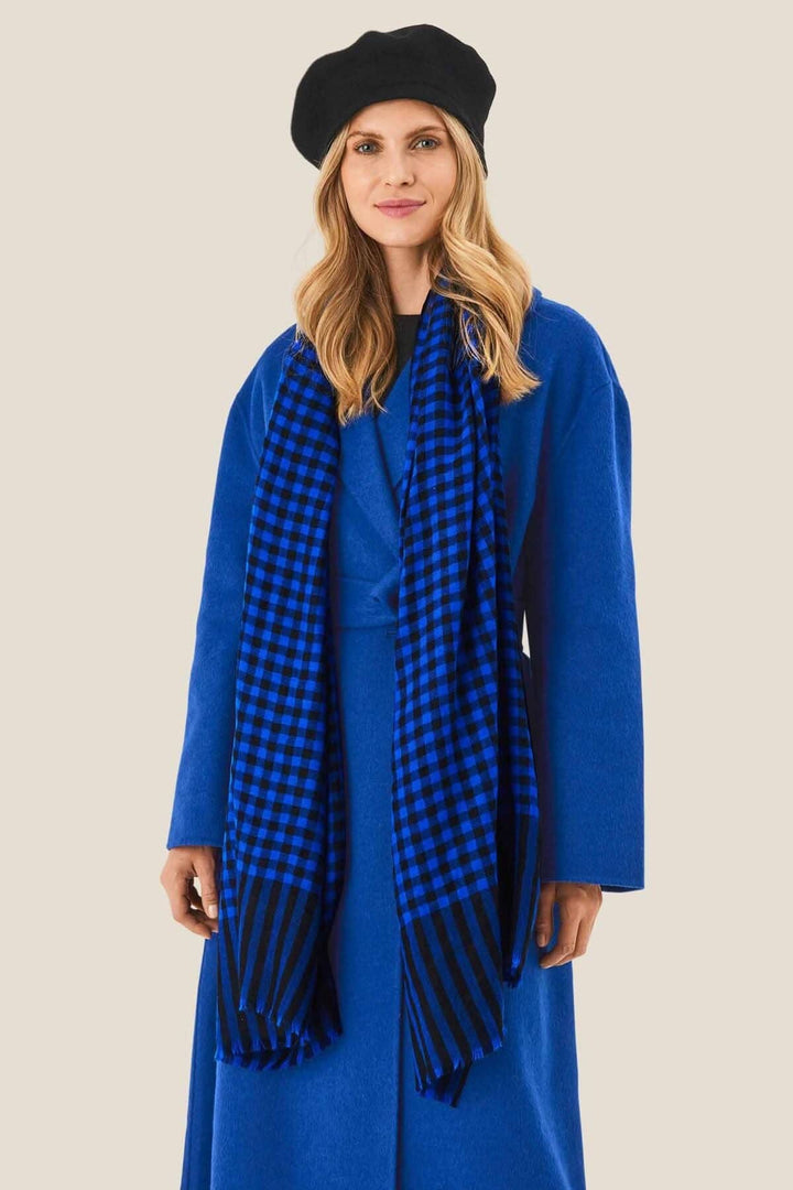 Foulard à carreaux noirs et bleus porté avec un manteau bleu et un béret noir, ajoutant du style et de la chaleur.