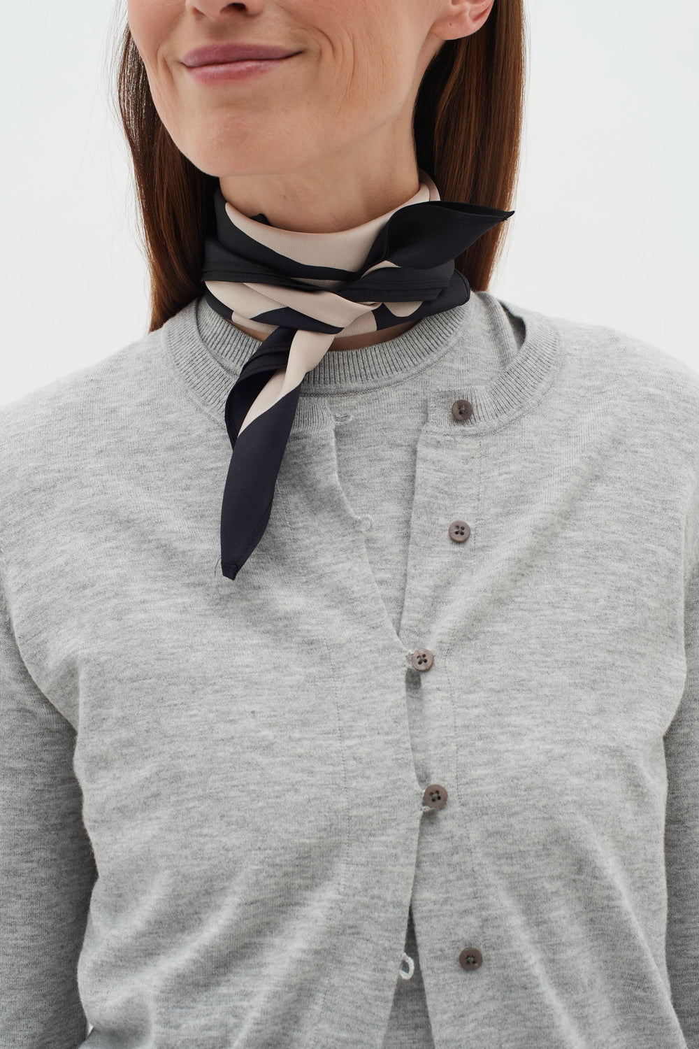 Foulard en soie Rafiq noué autour du cou, apportant sophistication à un pull gris.