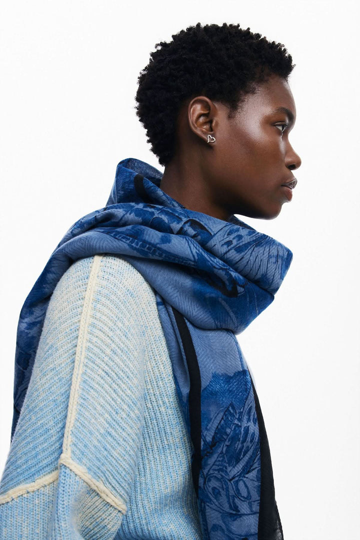Foulard papillon en bleu porté sur les épaules, ajoutant une touche dynamique à la tenue.