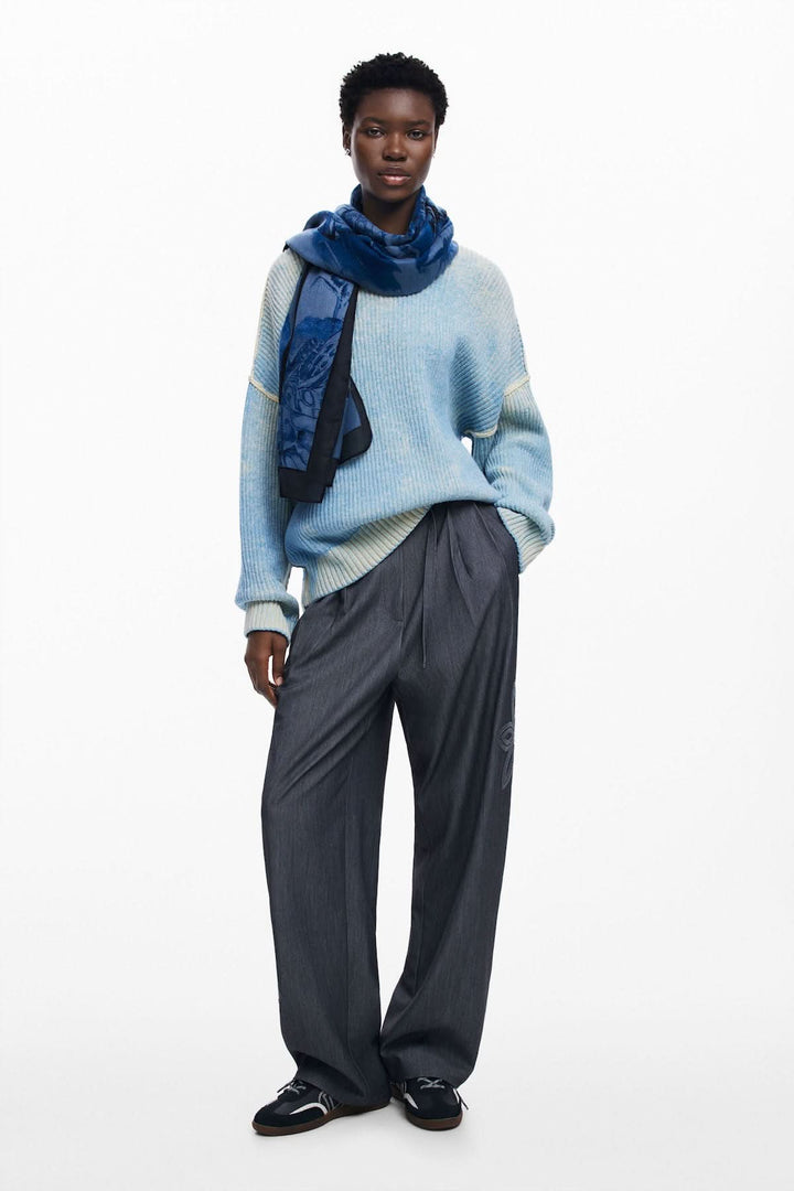 Mode féminine avec foulard papillon, pull bleu et pantalon gris, look chic et décontracté.