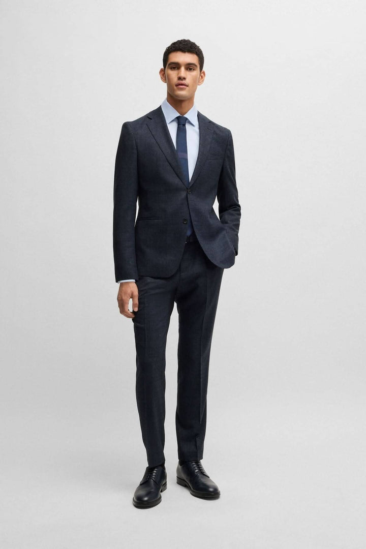 Homme en costume deux pièces BOSS moderne, noir, avec cravate, pose sobre sur fond neutre.
