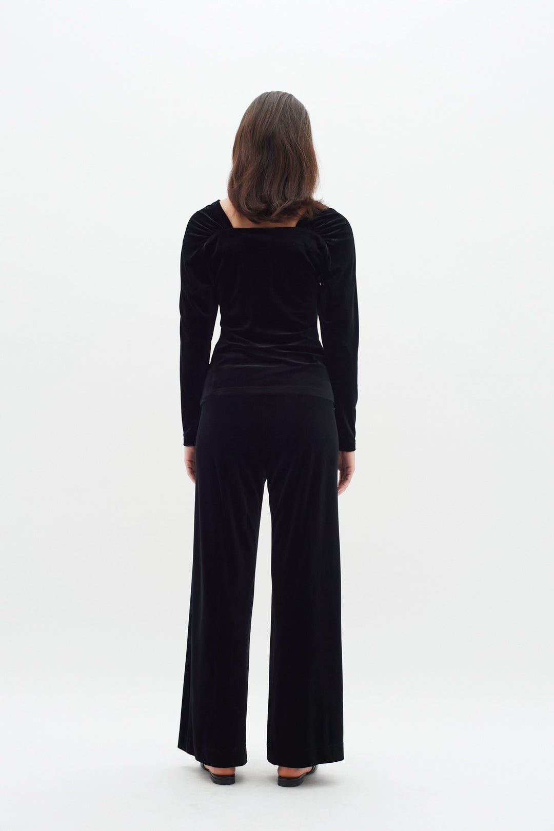 Femme vue de dos portant un haut en velours noir à col carré et pantalon assorti, style élégant et confortable.