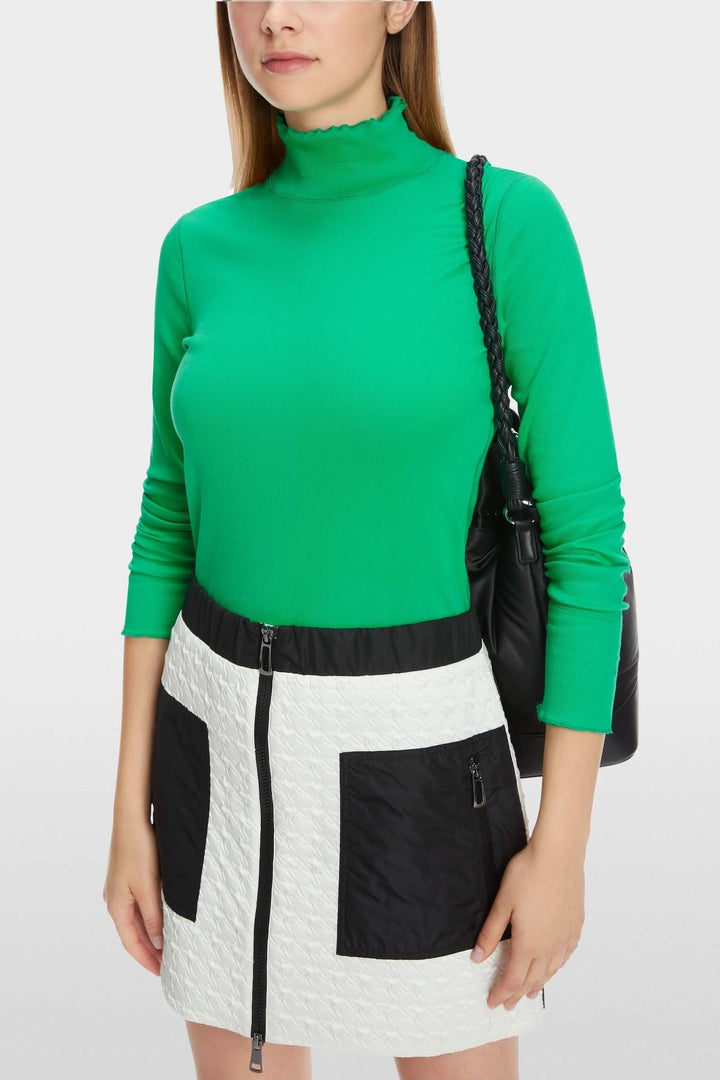 Haut col mock ajusté vert porté avec une jupe à poches en noir et blanc, parfait pour un look d'hiver chic.