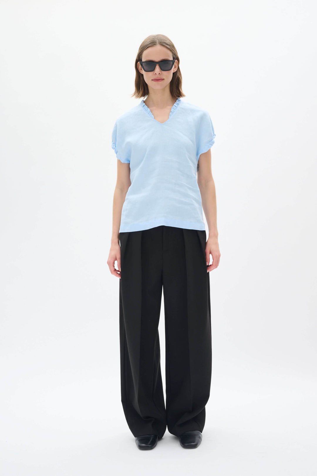 Haut en lin Rigitta en bleu clair avec encolure en V, manches courtes et pantalon noir élégant.