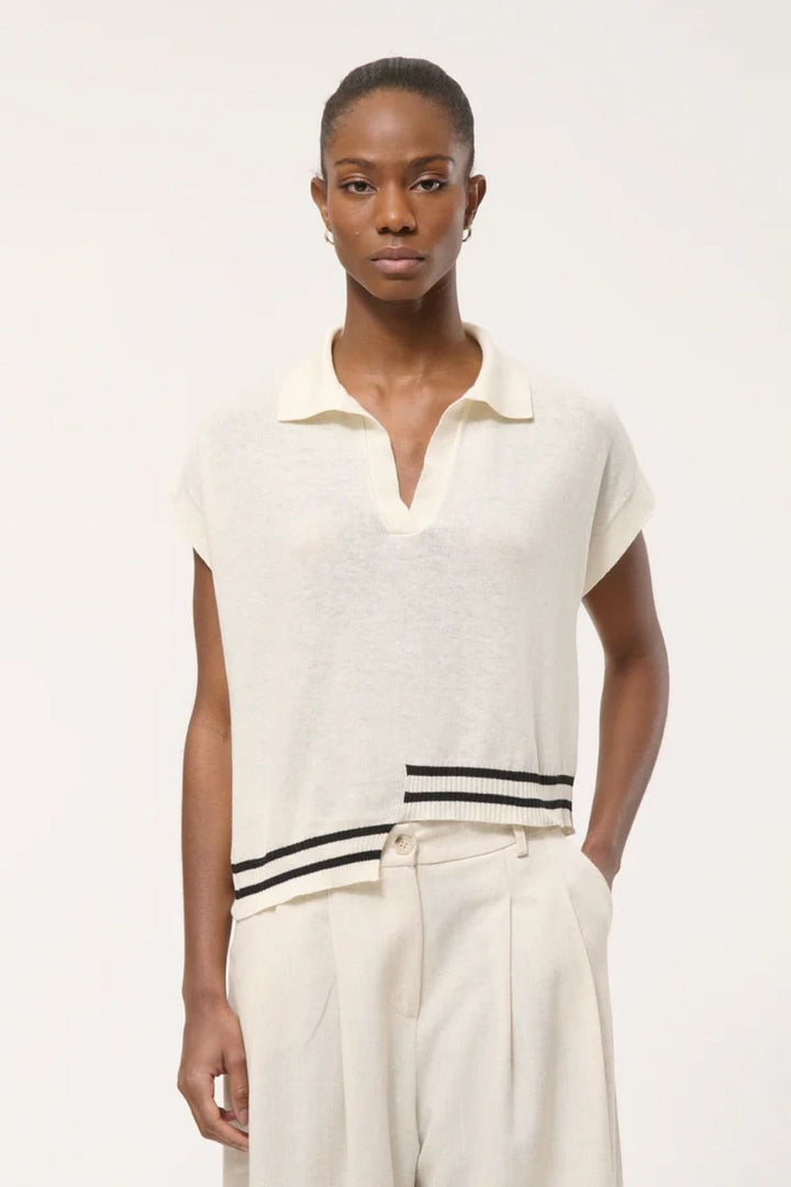 Modèle portant un haut en tricot à rayures contrastantes avec col polo ouvert, sur fond blanc.