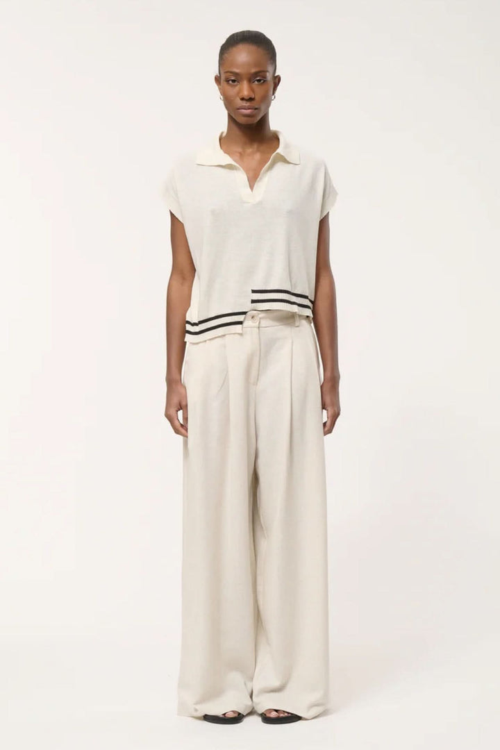 Femme portant un haut en tricot à rayures contrastantes avec un col polo ouvert et un pantalon ample.