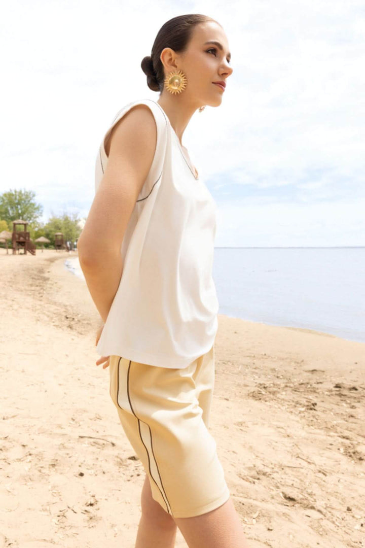 Femme portant un haut fluide col en V sur une plage, avec un style moderne et raffiné, idéal pour des tenues décontractées.