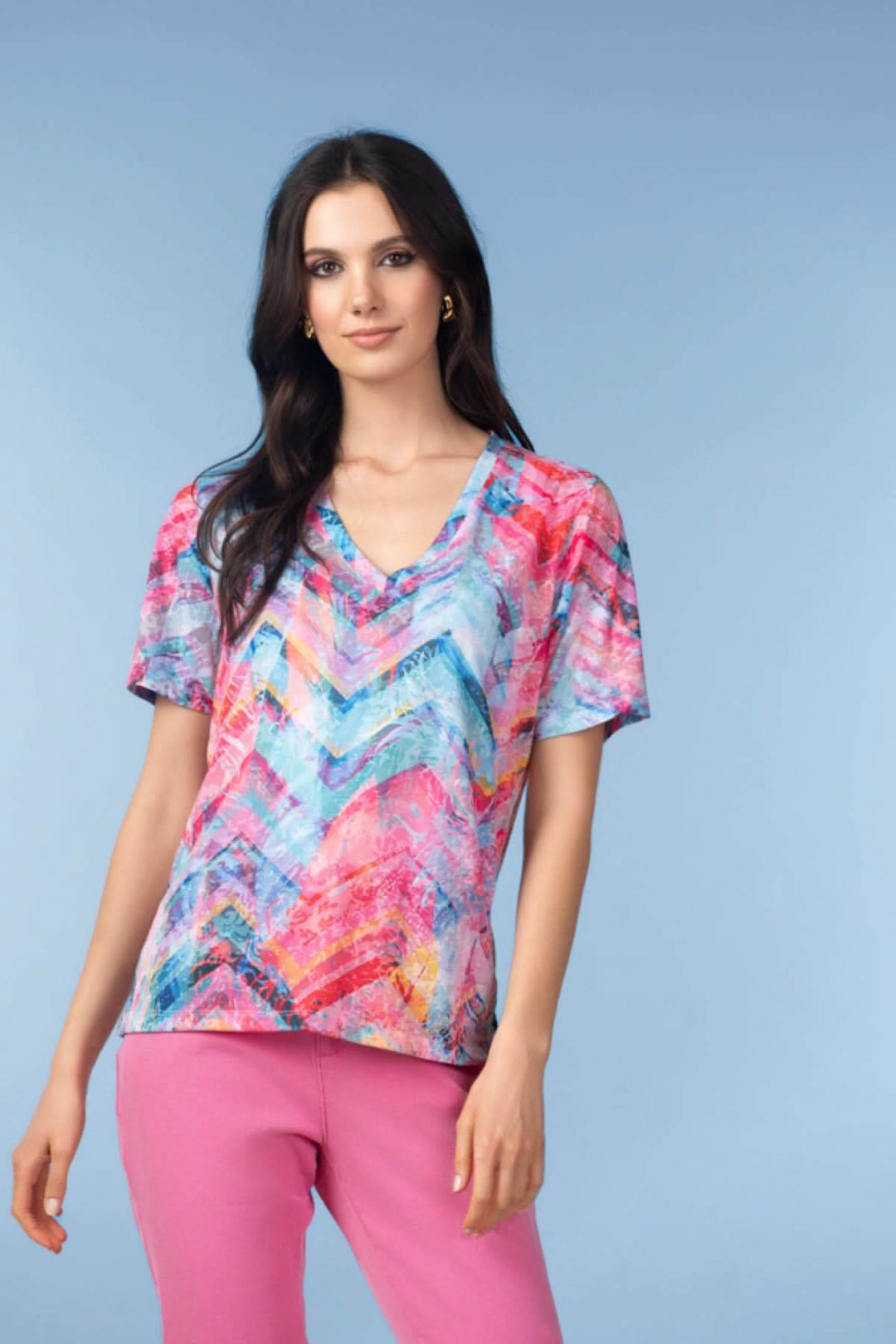 Haut imprimé graphique col V avec manches courtes et coupe fluide, porté par un mannequin sur fond bleu.