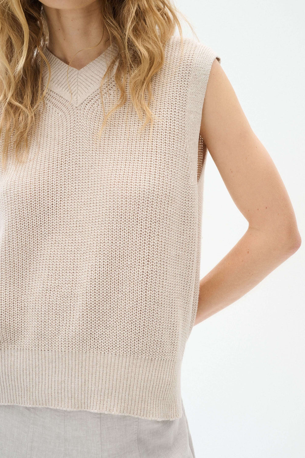 Pull sans manches en maille beige avec col en V, élégant et léger, parfait pour la mi-saison.