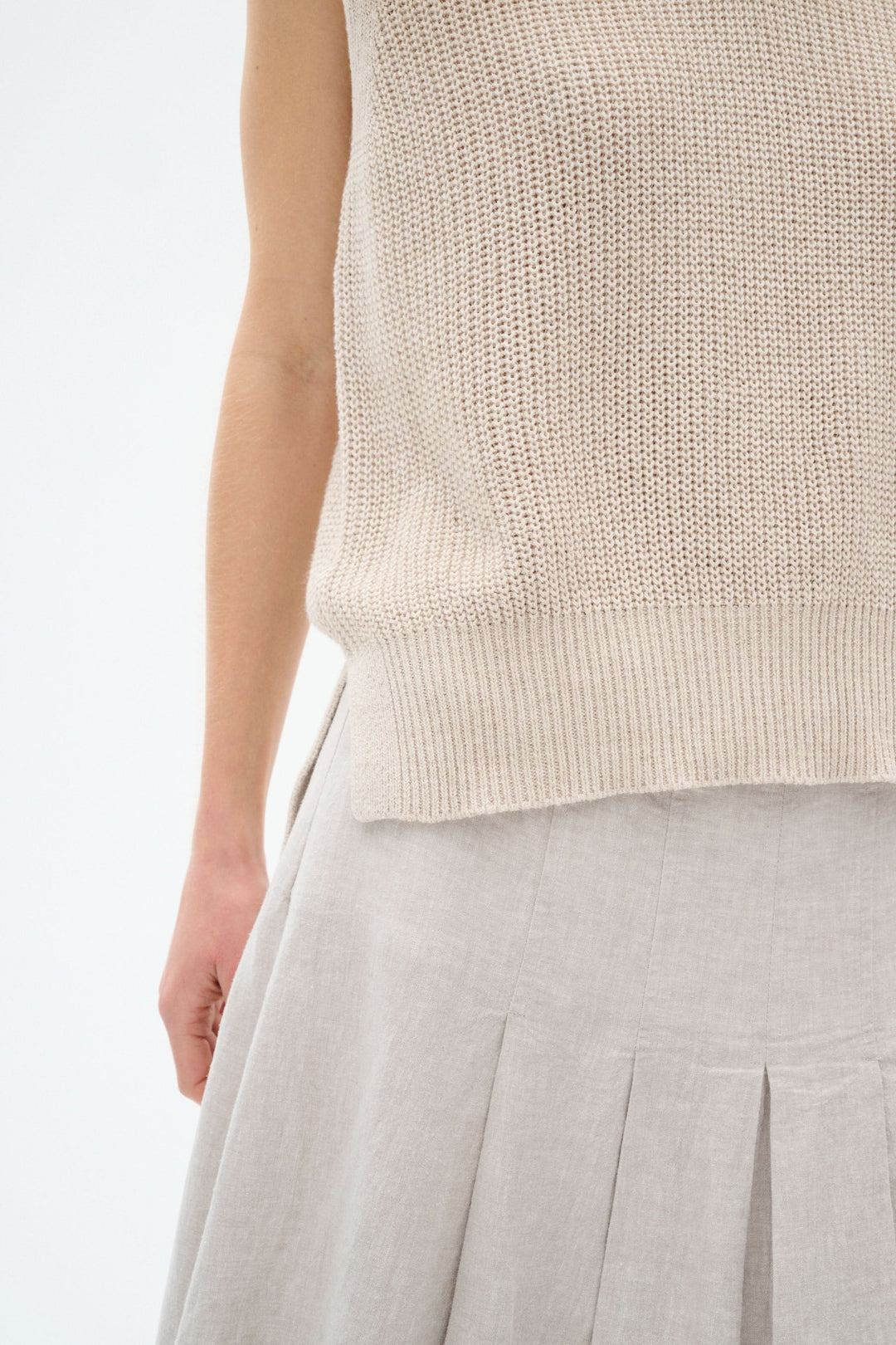 Pull sans manches en maille légère, couleur beige, stylé avec une jupe plissée en lin.