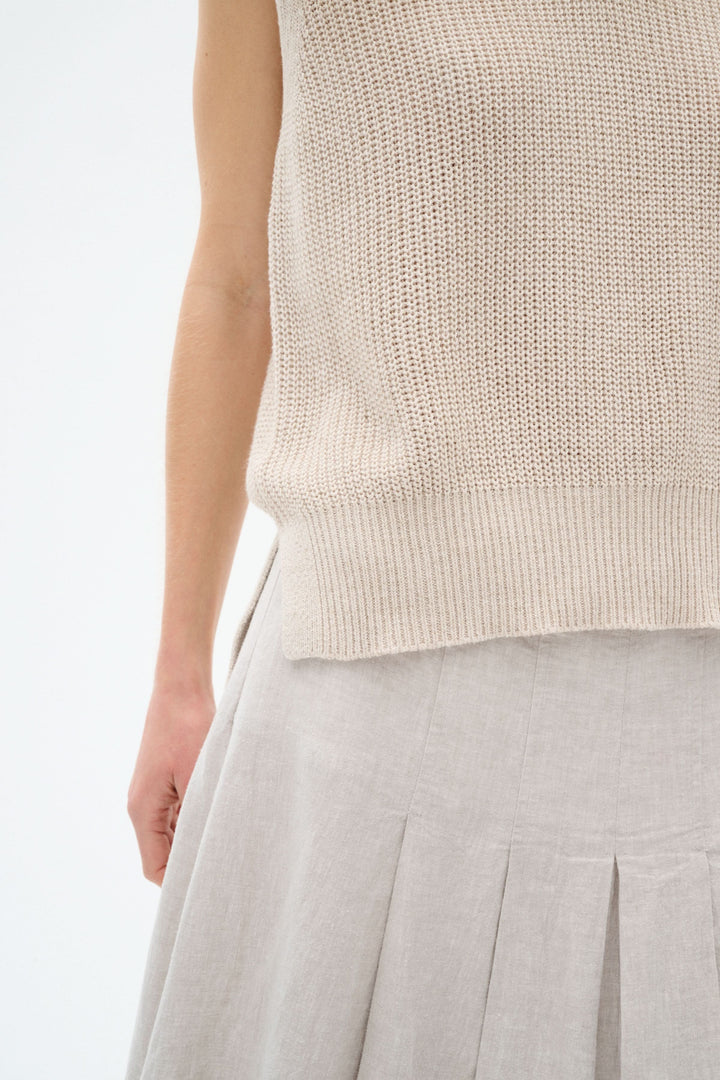 Pull sans manches en maille légère, couleur beige, stylé avec une jupe plissée en lin.