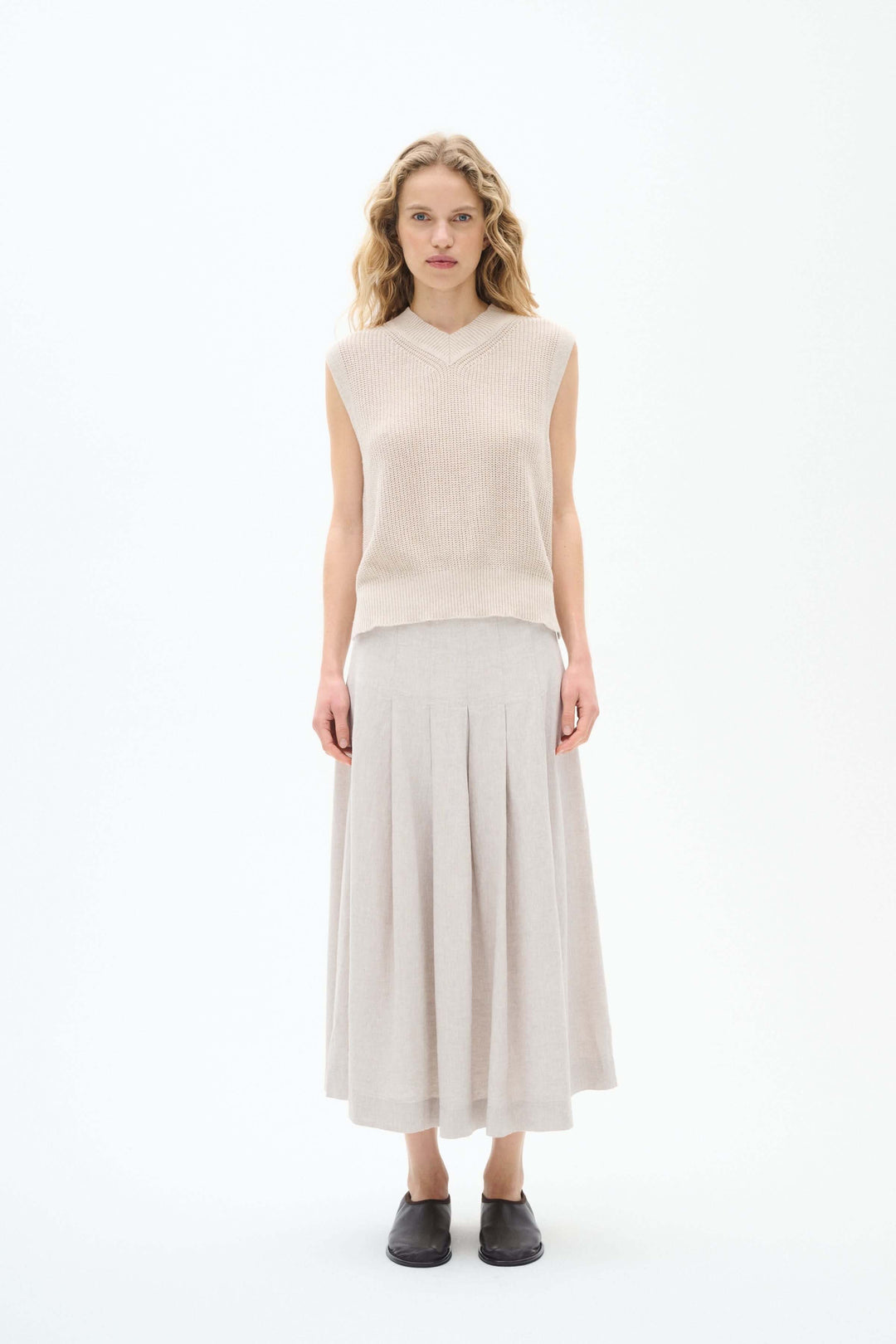 Femme portant un pull sans manches en maille beige avec une jupe longue plissée, style élégant et léger.