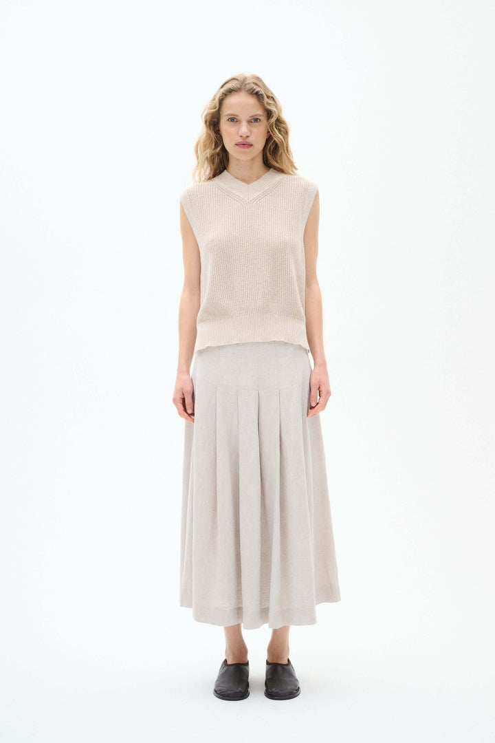 Femme portant un pull sans manches en maille beige avec une jupe longue plissée, style élégant et léger.