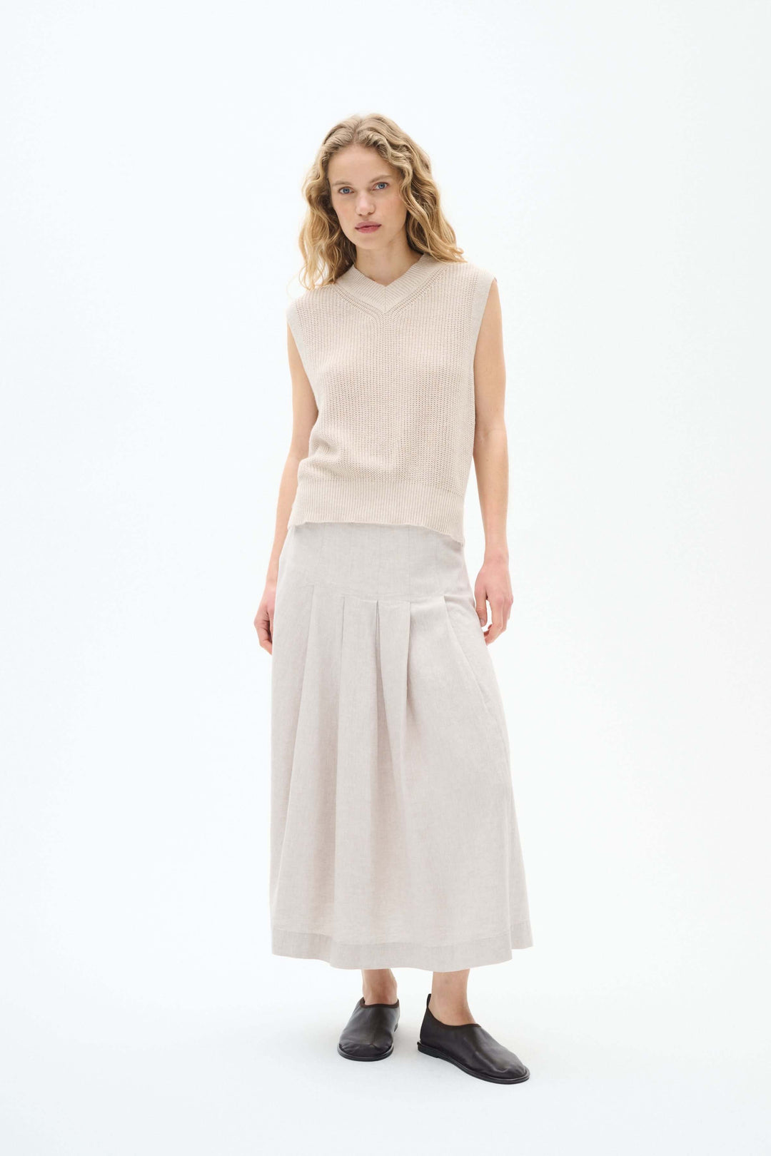 Pull sans manches en maille beige avec jupe longue et chaussures noires, idéal pour la mi-saison.