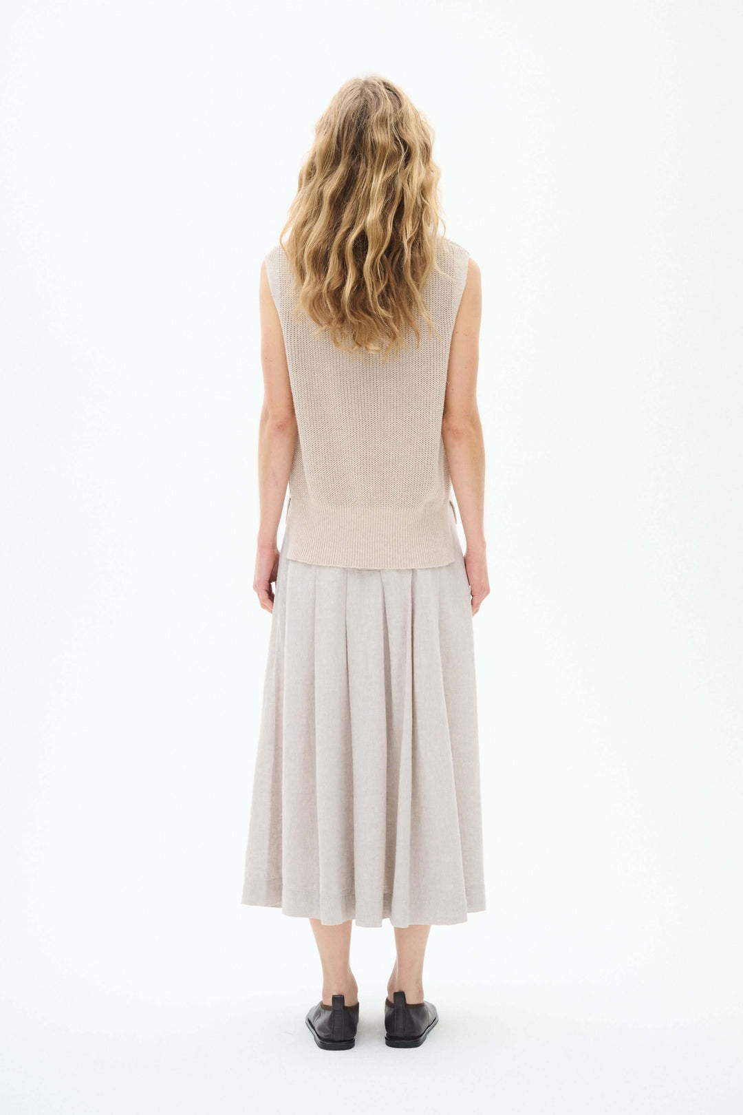 Femme voyant le dos d'un pull sans manches beige et jupes fluides, en tissu léger pour la mi-saison.