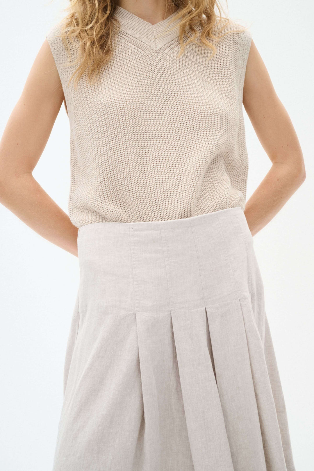Pull sans manches en maille beige avec encolure en V, porté avec une jupe beige élégante.