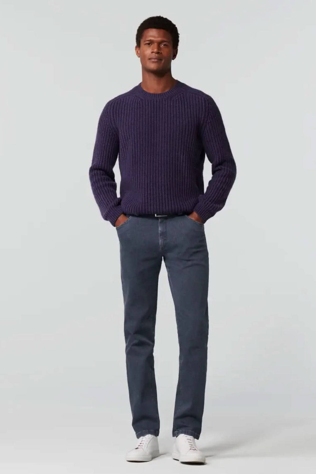 Homme portant un pull en maille violet et un jean slim en denim, avec des baskets blanches. Look décontracté et élégant.