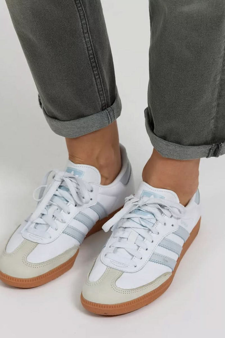 Baskets blanches avec rayures grises, portées avec un pantalon retroussé, style décontracté et tendance.