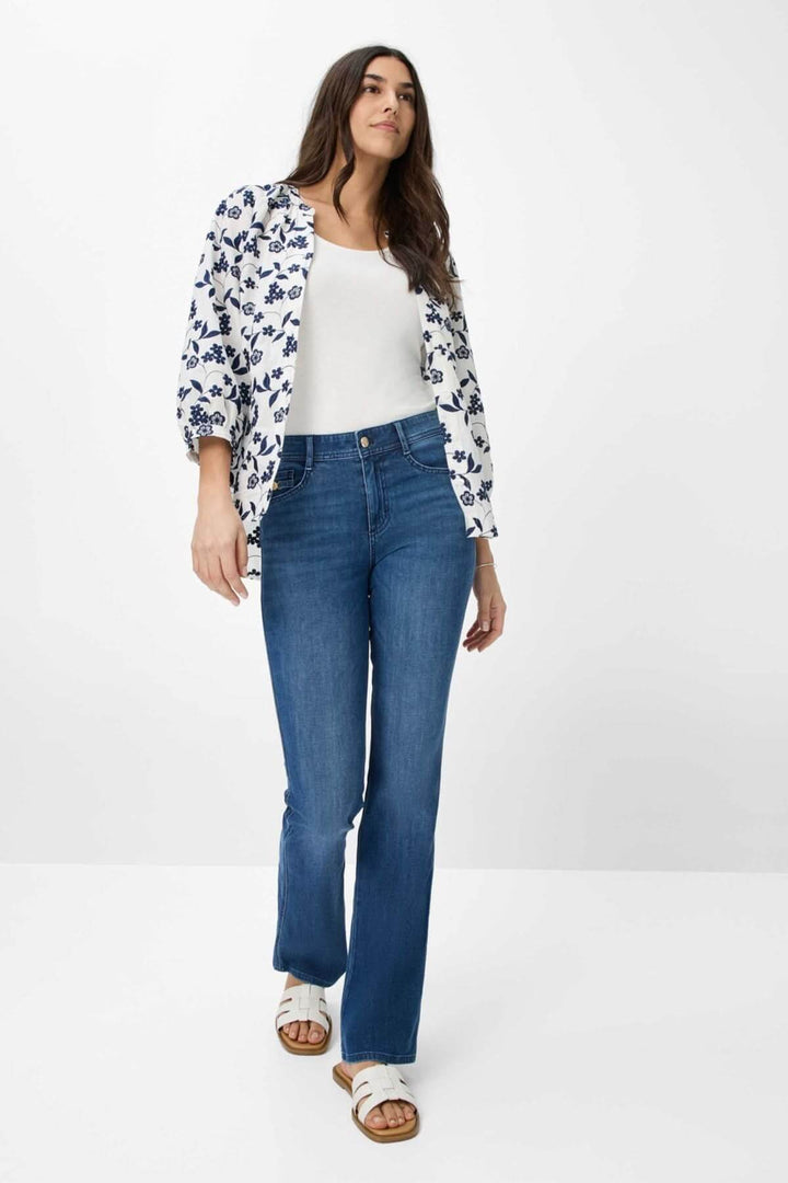 Femme portant le jean Shakira bootcut, alliant confort et style moderne, avec un haut blanc et un cardigan fleuri.