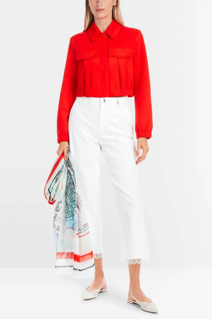Femme en blouse rouge avec pantalons blancs, tenant un foulard coloré, mettant en avant un look élégant.