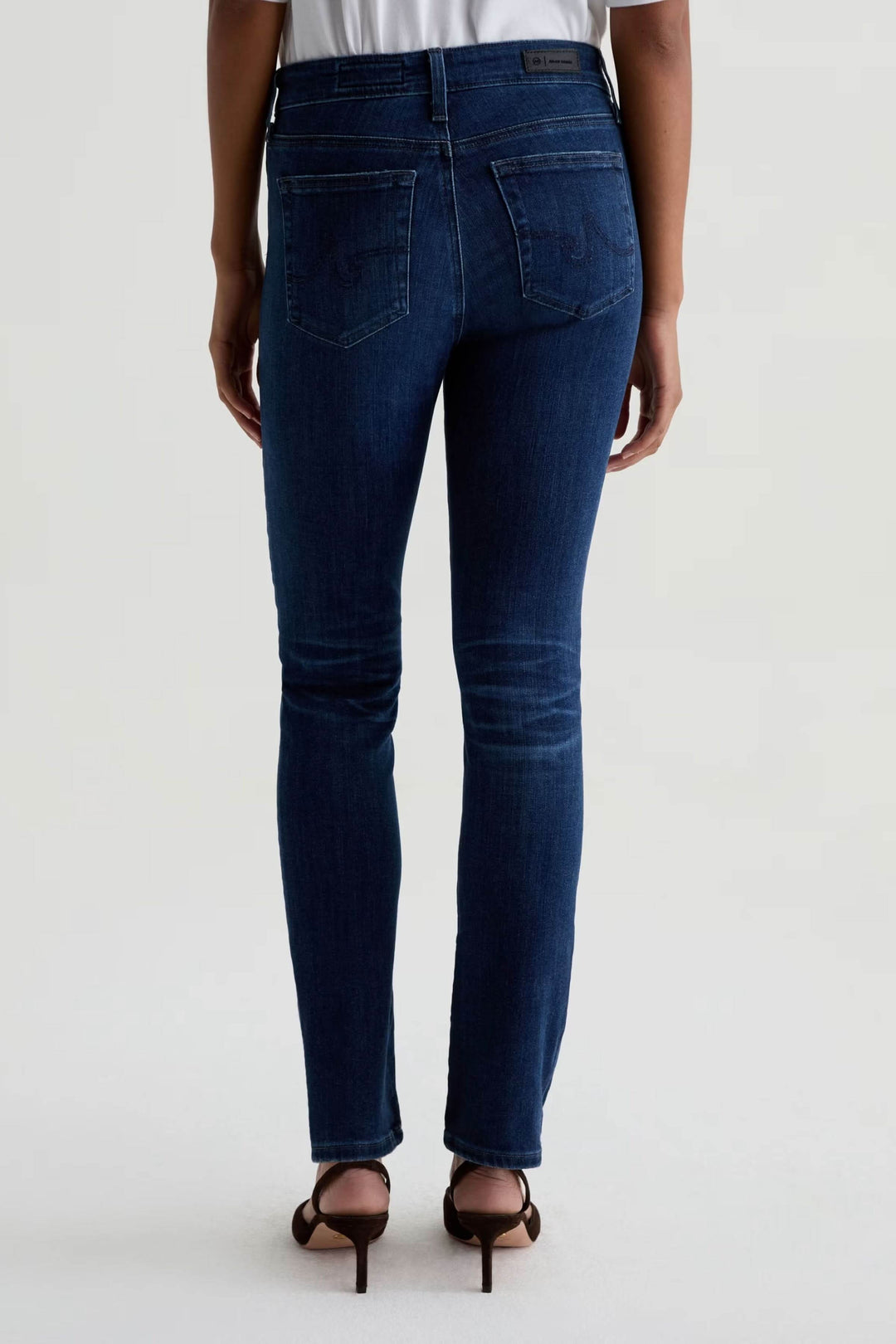 Jean ajusté à taille mi-haute en denim extensible, vue arrière, avec talons. Parfait pour un look décontracté-chic.