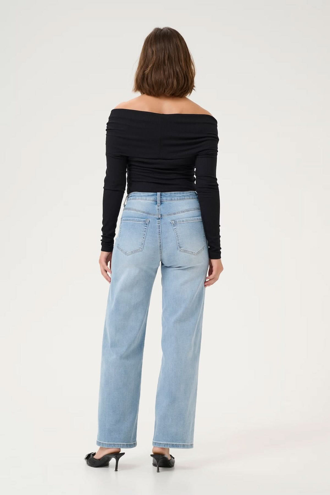 Femme portant un jean à coupe large avec une blouse noire, vue arrière, style moderne et confortable.