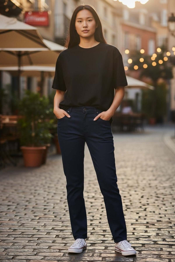 Jean slim à taille mi-haute porté par une femme dans la rue avec un t-shirt noir décontracté et des baskets blanches.