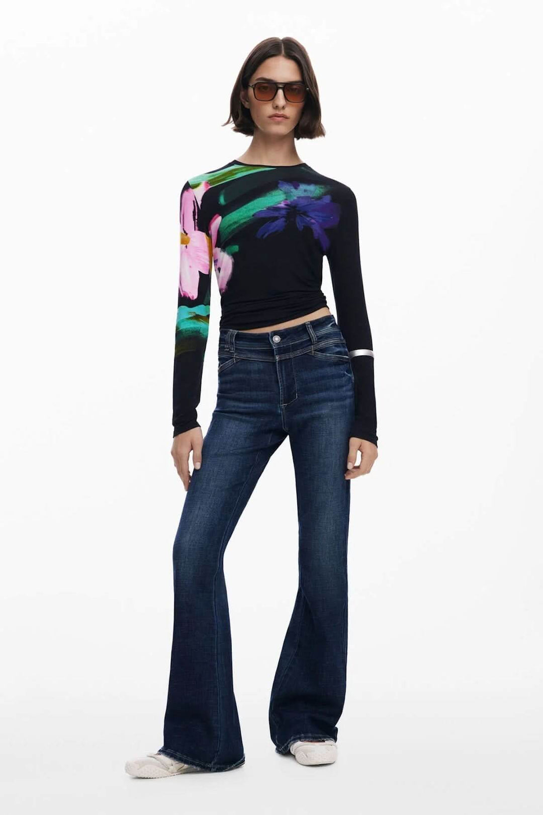 Jean évasé taille haute avec surpiqûres contrastantes et toile foncée, porté avec un haut à motifs colorés et lunettes de soleil.