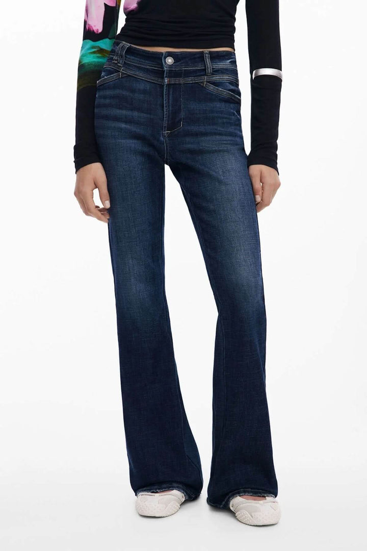 Jean évasé taille haute en toile foncée, coupe décontractée avec surpiqûres contrastantes, portée avec un haut ajusté, style chic.