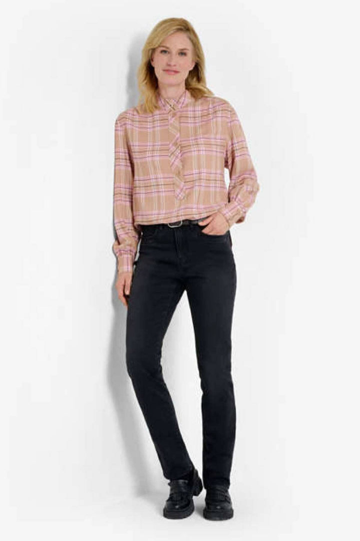 Femme en chemisier à carreaux et jean noir, offrant un look tendance et classique.