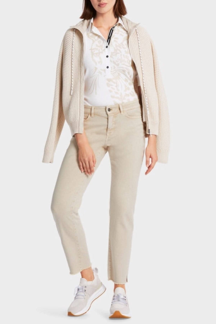 Femme portant un cardigan beige, polo à motifs et jeans clairs, avec des baskets blanches, dans un style décontracté.