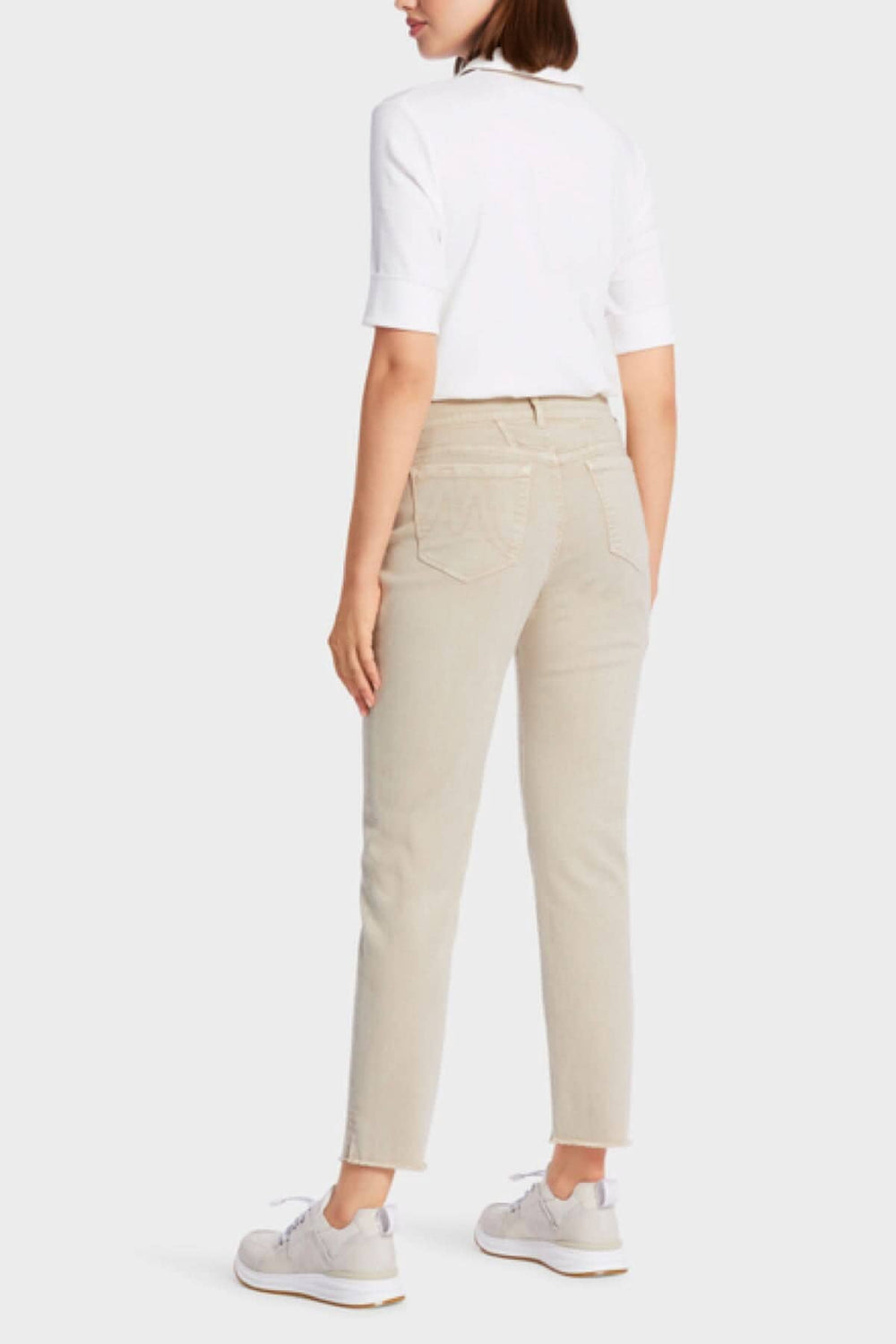 Femme portant des jeans SIKAR beige avec une blouse blanche et des chaussures blanches, vue de dos.