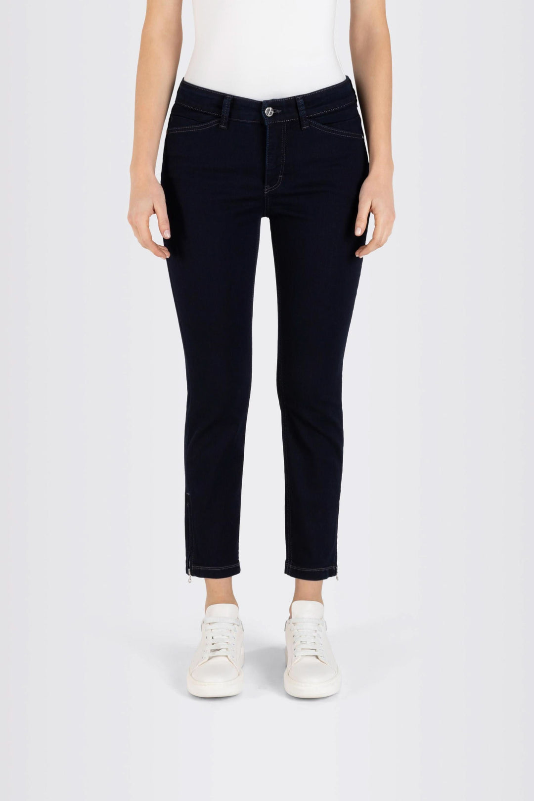 Jeans coupe ajustée longueur 7/8 en tissu extensible, taille régulière, fermés par bouton et fermeture éclair, avec sneakers blancs.