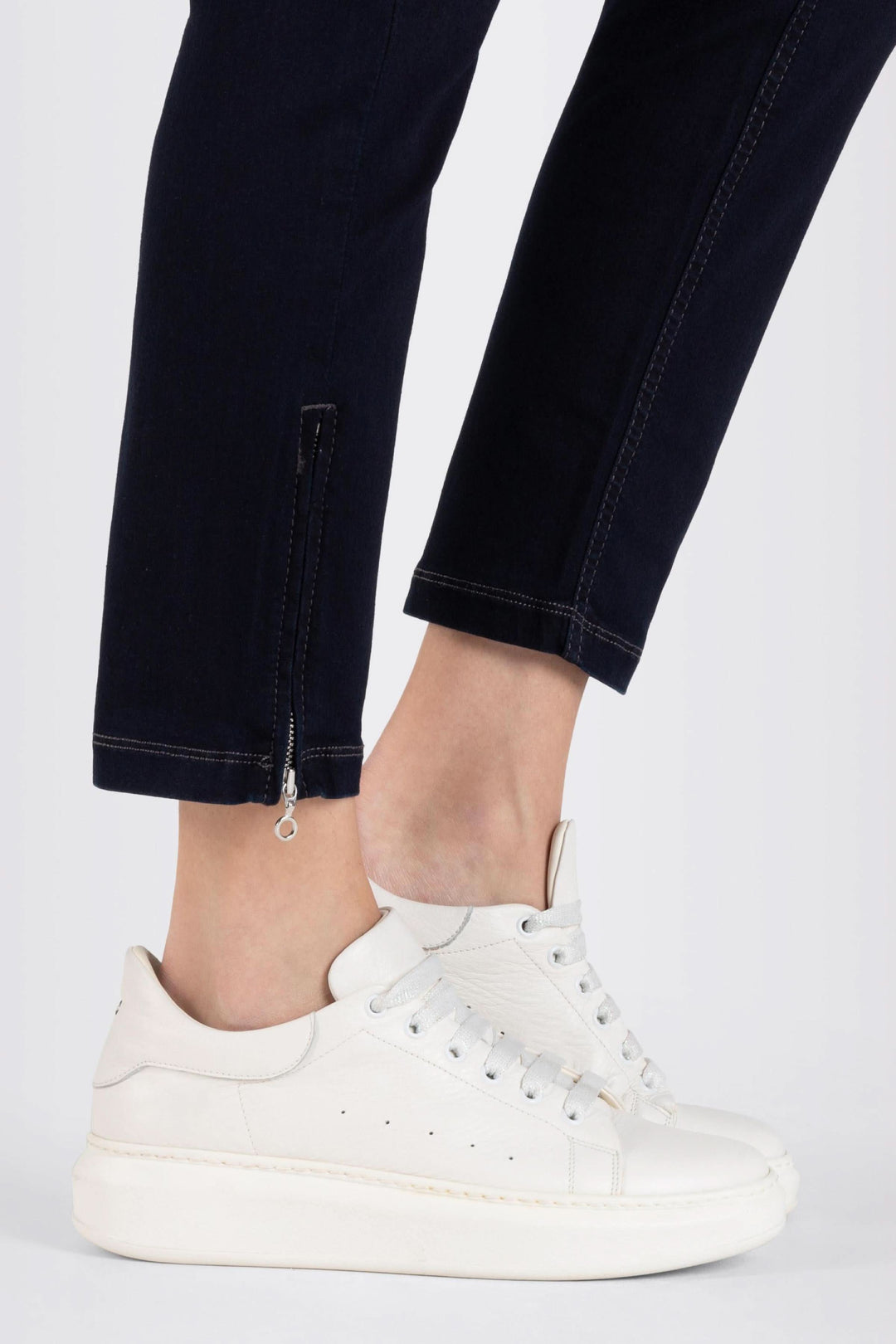 Jeans coupe ajustée longueur 7/8 avec chaussures blanches, dévoilant la cheville élégamment.