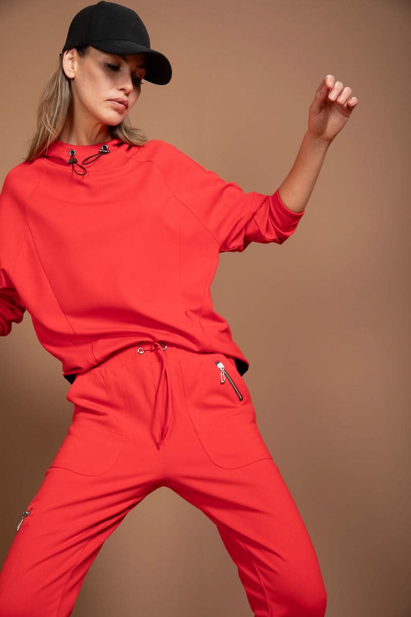 Femme posant en jogging ajusté rouge avec capuche et casquette noire, mettant en valeur le confort et le style utilitaire moderne.