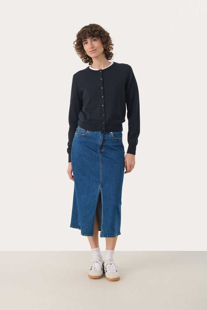Femme portant une jupe en denim midi avec fente frontale et un chandail noir, style urbain chic.