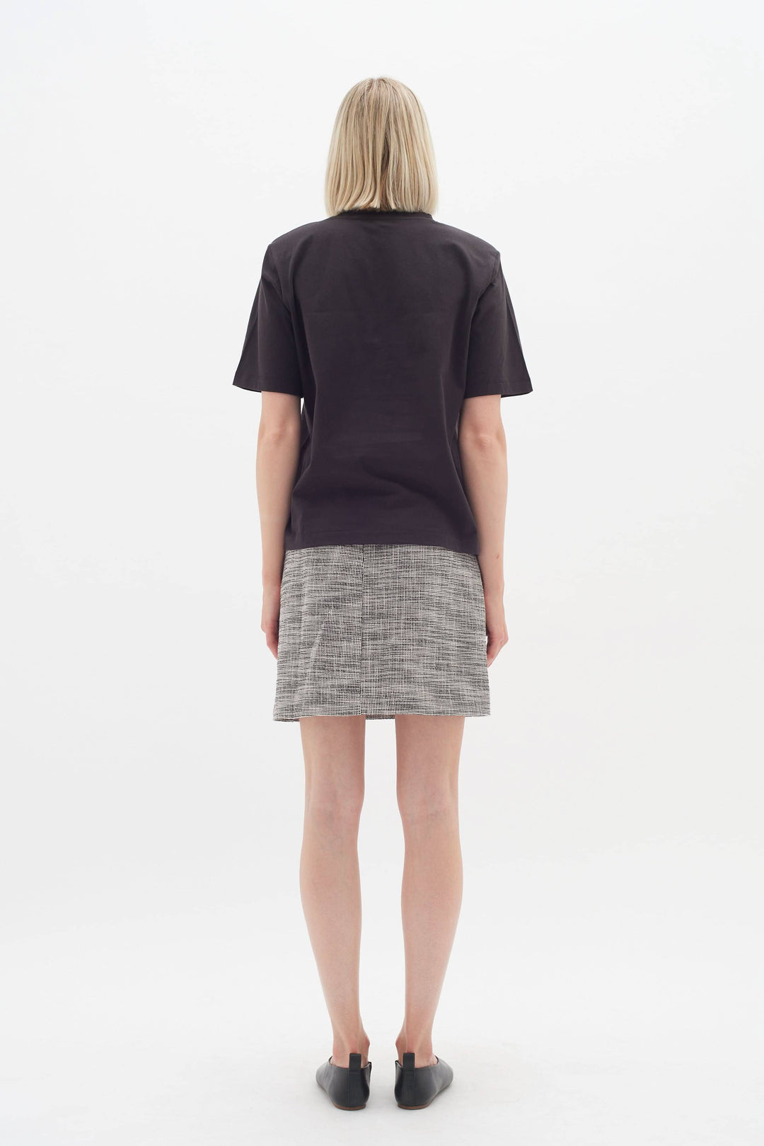 Femme vue de dos portant une jupe Zaccai à motif de carreaux et un t-shirt simple, idéale pour le bureau.