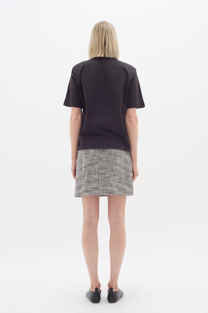 Femme vue de dos portant une jupe Zaccai à motif de carreaux et un t-shirt simple, idéale pour le bureau.