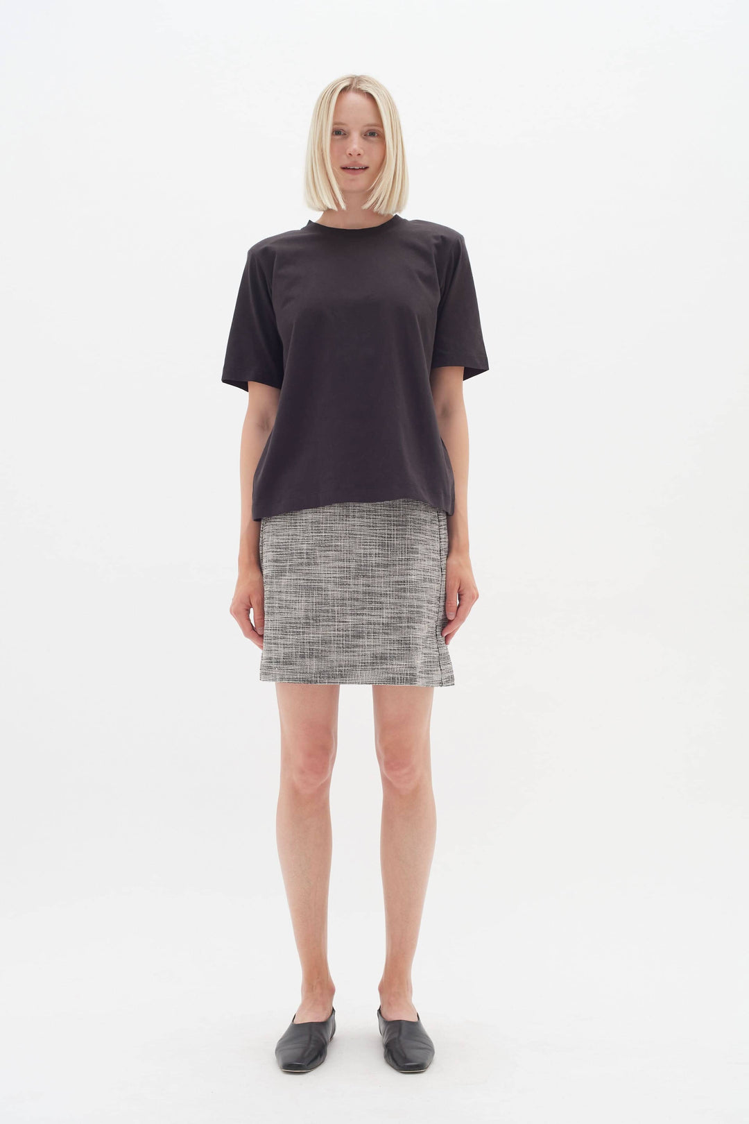 Femme portant une jupe à petits carreaux et un haut noir, pour un look professionnel au bureau.