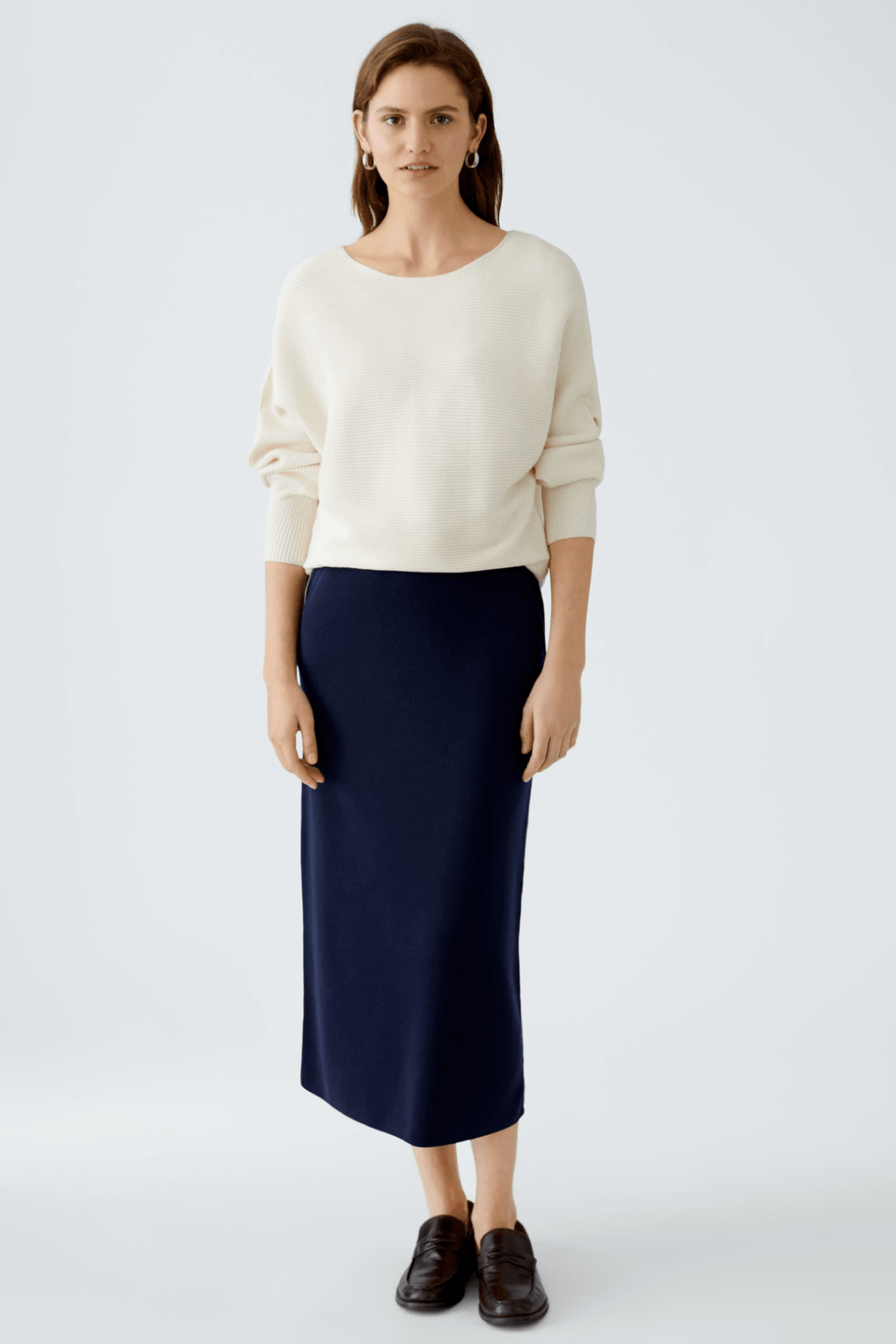 Femme portant une jupe droite en tricot navy avec un pull beige, style chic et décontracté.
