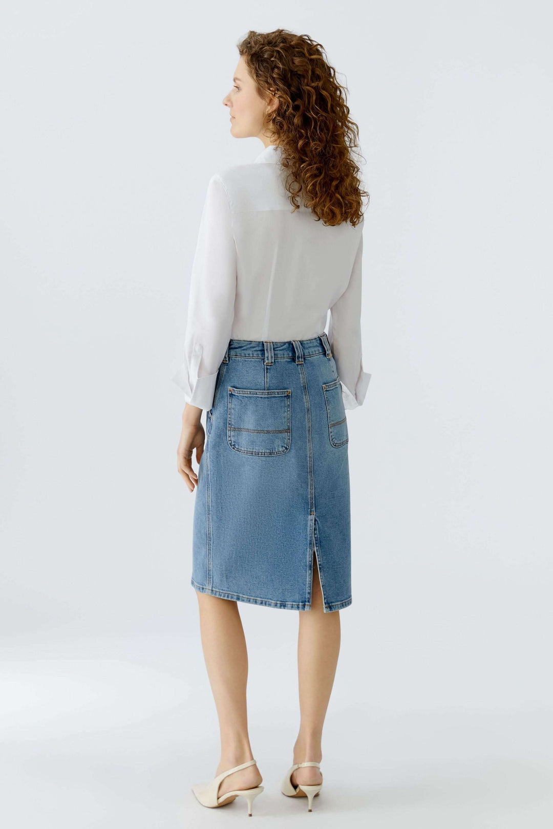 Jupe en denim classique vue de dos, silhouette structurée et élégante, longueur au genou, avec une blouse blanche.