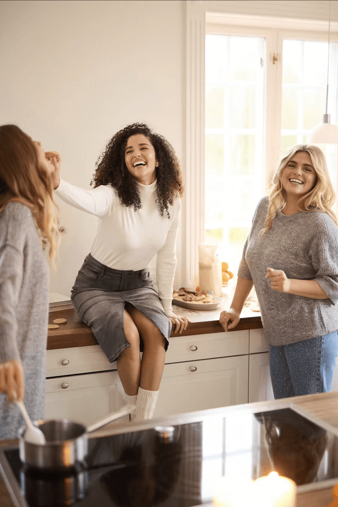 Trois femmes souriantes dans une cuisine, en train de cuisiner et passer un moment convivial ensemble.
