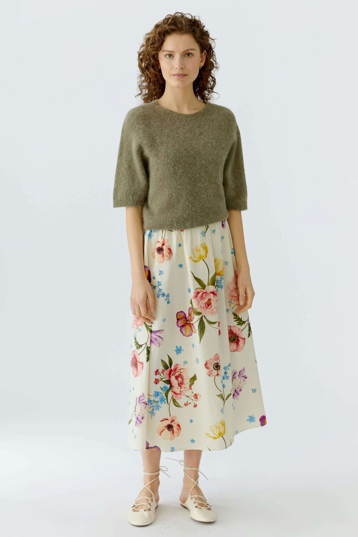 Femme portant une jupe mi-longue imprimé de fleurs avec un haut vert, offrant un style élégant et polyvalent pour toute occasion.
